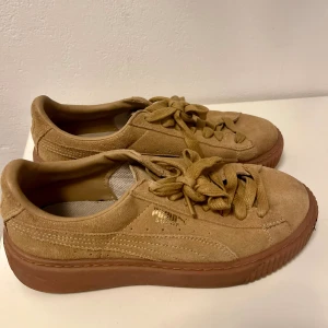 Puma Suede sneakers i beige mocka -  Puma Suede sneakers i beige mocka med tjock gummisula i brunt. Skorna har klassisk snörning och guldfärgad Puma-logga på sidan. 