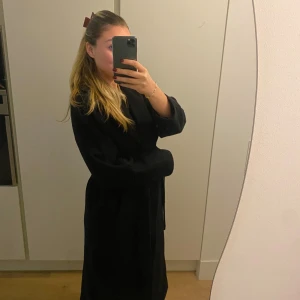 Svart kappa från Weekday - Svart kappa med knytband i midjan. Kappan har en klassisk krage och långa ärmar. Ullblandning. Fint skick!