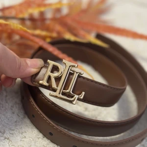 Brunt skärp från Ralph Lauren - Snyggt brunt bälte från Ralph Lauren med en stilren RL-spänne i guldmetall. 110Cm