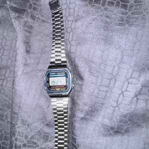 Casio digital klocka silver - Casio digital klocka med klassisk rektangulär display och silverfärgad länkarmband i metall. Klockan har funktioner som alarm, kronograf och bakgrundsbelysning. Tydlig LCD-skärm med blå och röda detaljer runt displayen. Och man kan ändra storleken enkelt så den passar 