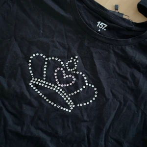 Svart t-shirt  - Svart t-shirt från 157 i storlek S med ett glittrigt strassmotiv av en krona och ett hjärta på bröstet. Klassisk rund hals och korta ärmar. Tröjan är i grund från lager 157, går att tvätta OBS! Bara i 30 grader, ingen torktumling 