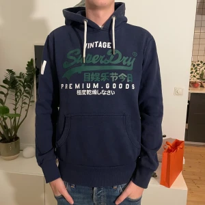 Mörkblå Superdry hoodie - Snygg superdry hoodie i storlek L men sitter mer som M. Modellen är 187cm. Skriv vid funderingar