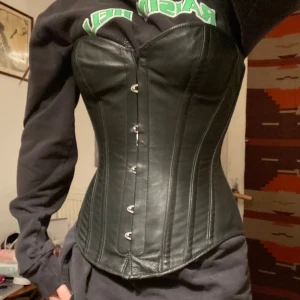 Svart skinnkorsett med snörning - svart korsett i skinnimitation med metallknäppning framtill. Baksidan har justerbar snörning. riktigt bekväm och bra kvalitet. passar nog S möjligtvis M och XS. kupan ca C