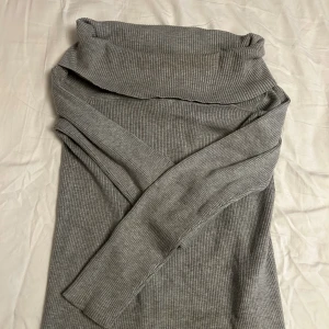 Grå - offshoulder ribbad långärmad tröja - Snygg grå ribbad tröja med lång ärm och bred polokrage. Den är figurnära och har en mjuk, stickad känsla som gör den både bekväm och stilren. Perfekt för dig som gillar minimalistisk och clean look.