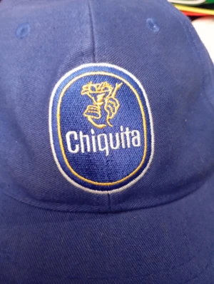 Blå Chiquita keps med broderad logga - Snygg blå keps från Chiquita med broderad logga framtill i vitt och gult. Klassisk form med böjd skärm och ventilerande hål upptill. Perfekt för dig som vill sticka ut med en unik och cool accessoar. Tillverkad i bomull för skön passform.