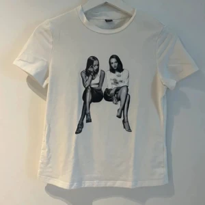 Vit t-shirt med grafiskt tryck - Vit t-shirt med coolt grafiskt tryck av två sittande tjejer i svartvitt. Klassisk rund hals och korta ärmar. Passformen är normal och materialet känns som mjuk bomull. Perfekt för dig som gillar statement-plagg med unik design.