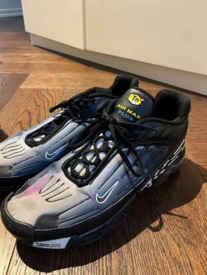 Nike Air Max Plus svarta sneakers - Nike Air Max Plus sneakers i svart och grått med coola detaljer och snörning. Snyggt TN-märke på plösen och Tuned Air-text på sulan. Skorna har en sportig design med platt sula och små vita swoosh-loggor på sidorna. Storlek 42