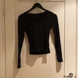 Svart ribbad långärmad topp Lindex XS - Svart långärmad topp från Lindex i storlek XS. Ribbad struktur och rund halsringning med söt spetskant. Materialet är mjukt och stretchigt, perfekt för en chill och stilren look. Ärmarna har samma spetsdetalj som halsen för extra vibe.