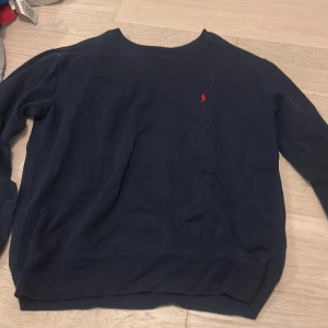 Mörkblå sweatshirt från Polo Ralph Lauren - Snygg mörkblå sweatshirt från Polo Ralph Lauren med klassisk röd logobrodering på bröstet. Tröjan har rund hals och långa ärmar, perfekt för dig som gillar stilrena och tidlösa plagg. Mjuk bomullskvalitet som är skön att ha på sig.
