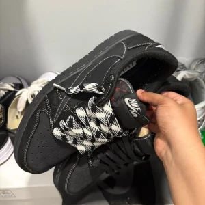 Nike Jordan 1 svart mocka sneakers  - Dessa Air Jordan 1 x Travis Scott har en snygg svart mocka med vita sömmar som gör att skorna står ut. De svartvita skosnörena har ett rutigt mönster som ger en cool detalj. Skorna är låga, har rund tå och en platt sula som är skön att gå i.