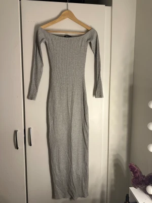 Grå ribbad långklänning offshoulder - Säljer en snygg grå långklänning med ribbad struktur och offshoulder-design. Klänningen har lång ärm och sitter tight mot kroppen för en stilren look. Perfekt för dig som gillar minimalistisk stil och vill ha något som sticker ut.
