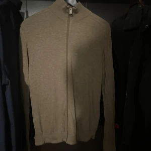 Stickad Full zip tröja - Snygg beige polotröja med hel dragkedja framtill och långärmad design. Tröjan har en stilren och enkel look med hög krage, perfekt för lager-på-lager. Materialet känns mjukt och lätt, vilket gör den skön att bära under kyliga dagar.