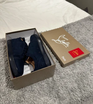 Christian Louboutin Mörkblåa mocka  - Snygga mörkblå sneakers från Christian Louboutin i mjuk mocka med klassisk röd sula och broderad logga på baksidan av skon, Skorna är helt nya säljer då jag råkade köpa fel storlek, billigare vid snabb och smidig affär