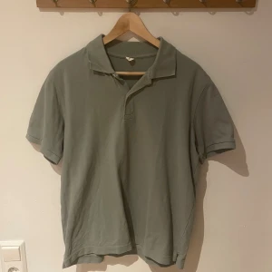 Grön pikétröja från Arket i bomull, storlek M - Snygg grå pikétröja i klassisk modell med krage och korta ärmar. Tillverkad i mjuk bomull som känns skön mot huden. Perfekt för en avslappnad och stilren look. Passar dig som gillar enkel och tidlös stil.