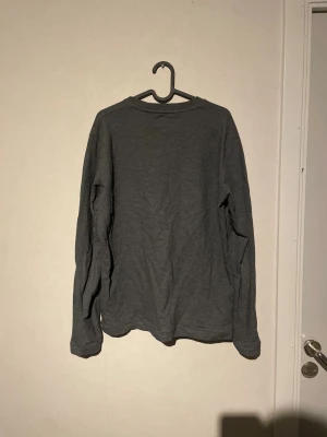 Grå långärmad tröja från Marc O'Polo - En enkel och stilren grå långärmad tröja från Marc O'Polo. Tröjan har rund hals och är gjord i mjuk bomull, perfekt för chill dagar eller när du vill ha en clean look. Passformen är normal och materialet känns skönt mot huden.