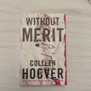 Without Merit - En bok med ett unikt omslag där säkerhetsnålar och röd tråd håller ihop ett rivet papper. Skriven av Colleen Hoover, en bästsäljande författare. Perfekt för dig som gillar starka berättelser och känslor. Passar unga vuxna som söker något annorlunda och tankeväckande.