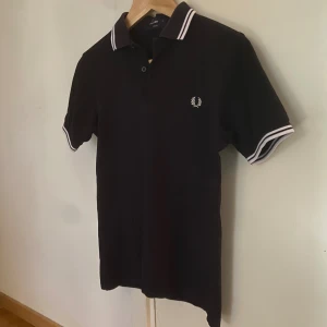 Fred Perry piké - Sjukt snygg marinblå Fred Perry piké/polo tröja. Köpte den för några månader sedan, men har växt ur den. Tröjan har inga defekter och är inprincip i nyskick! Den är i storlek XS.
