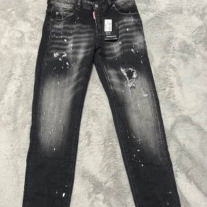Svarta Dsquared2 jeans med slitningar - Svarta jeans från Dsquared2 med coola slitningar och färgstänk på både fram- och baksida. Skinny fit med klassisk femficksdesign och tydliga detaljer som trasiga partier och blekta effekter. Tillverkade i Italien av jeansmaterial.