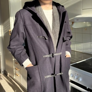 Mörkblå rock med luva - Säljer denna feta mörkblå rock med huva. Jackan har stora fickor framtill och vinrött innerfoder. Tillverkad i England och gjord i ullblandning, perfekt för kalla dagar. Modellen är 181cm och väger 72kg. Tveka med prisförslag.