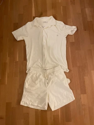 Vitt frottéställ Home of Ess - Säljer ett par vita shorts och piké från Home of Ess i storlek XL. De är gjorda i mjuk frotté, har elastisk midja med snörning och en bakficka. Perfekta för chill dagar eller när du vill ha något riktigt bekvämt på dig. Aldrig använda 