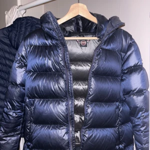 Mörkblå pufferjacka från Colmar - Säljer en mörkblå pufferjacka från Colmar med huva och snygg glansig finish. Det är en dunjacka som är väldigt varm och rymlig. På mig sitter jacka lite lösare eftersom jag valde ta en större storlek för att den skulle passa i längden. Fördel att man kan ha något tjockare under. Hör av er vid frågor! Nypris 6999kr