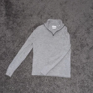 Grå halvzip merinoulltröja från These Glory Days - Säljer en stilren grå tröja i merinoull från These Glory Days. Tröjan har en dragkedja vid halsen och långa ärmar, perfekt för kyligare dagar. Den är mjuk och bekväm, idealisk för både vardag och mer avslappnade tillfällen. Storlek M men passar mer S 