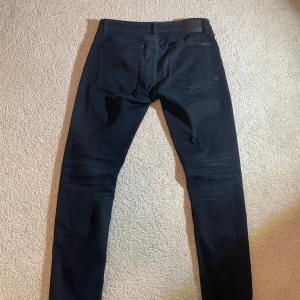 Svarta  jeans från Nudie Jeans | W34 L30 - Svarta jeans från Nudie Jeans i skinny fit med klassisk femficksdesign. Byxorna är tillverkade av 91% bomull, 6% polyester och 3% elastan för en skön stretch. Snyggt minimalistisk look och passform som sitter tajt längs benen.