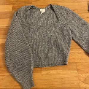 Grå ribbad stickad topp H&M - Grå croppad stickad topp från H&M med fyrkantig urringning och långa ärmar. Ribbstickat material som ger en snygg struktur.