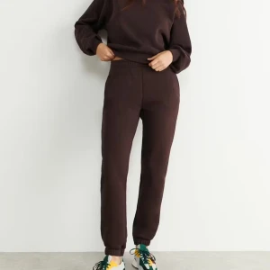 Gina Tricot Basic Sweatpants - Mörkbruna mjukisbyxor med elastisk midja och muddar vid bensluten. Byxorna har en relaxed passform och är tillverkade i mjukt bomullsmaterial, perfekta för chill dagar. Snygg och enkel design utan synliga loggor eller detaljer.