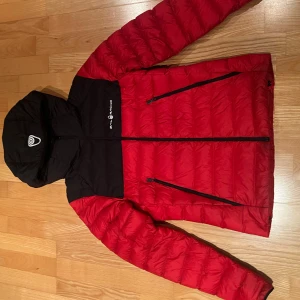 Tun dunjacka  - Säljer en höst/vår dunjacka av märke Sail racing, jackan är röd med en svart luva den är i bra skick används ett fåtal gånger med storlek xs.