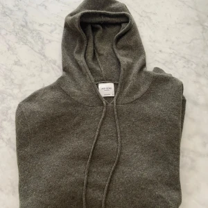 John Henric Kashmir hoodie (mörkgrön) - Snygg mörkgrå hoodie från John Henric i mjuk kashmir. Tröjan har huva med snörning, långa ärmar och en klassisk magficka. Perfekt för dig som gillar stilren och chill look med lyxig känsla.