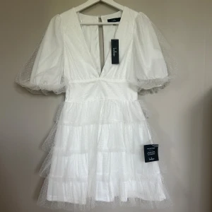 Vit kort klänning med puffärm från Lulus - Vit klänning från Lulus med puffiga korta ärmar och djup v-ringning. Klänningen har flera lager volanger i tyll med prickigt mönster. Nypris 1050