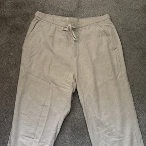 Beiga sommarbyxor med snörning från Zara - Snygga beiga linnebyxor från Zara med avslappnad passform och elastisk midja med snörning. Byxorna har sidfickor och raka ben, perfekta för en chill och stilren look. Materialet är svalt linne som passar grymt under varmare dagar.