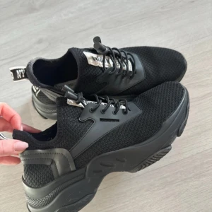 Svarta chunky sneakers Steve Madden - Svarta chunky sneakers från Steve Madden med grov sula och mesh-ovandel. Skorna har svarta snören med snabbstängning, detaljer i syntet och coola logoband bak. Perfekta för dig som gillar sportig och trendig stil. Passar även 39