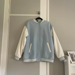 Ljusblå och vit bomberjacka - Baseball jacka ifrån H&M divided i storlek S. Filtyg med vitt konstskinn på armarna. Lite lätt fodrad och är i ljusblått med vita ärmar och detaljer. Jackan har ribbade muddar med ränder, tryckknappar framtill och två fickor. Denna är i nyskick då jag aldrig använt den🩵