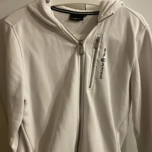 Vit Sail Racing  - Vit zip hoddie från  Sail Racing med huva och dragkedja framtill. Använd ca 3-4 gånger, kommer inte till användning. Den är i storlek 176.,som är ungefär som en M 