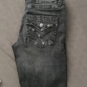 Svarta jeans från Gina Tricot, stl 164 - Snygga svarta jeans från Gina Tricot med coola detaljer på bakfickan och silvrig knapp framtill. Jeansen har klassisk femficksdesign och är tillverkade i ett mjukt denimtyg som sitter skönt hela dagen.
