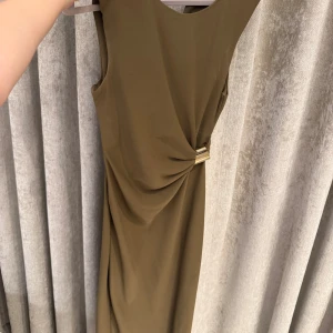 Klänning Zara - Vacker olivgrön klänning med guldigt spänne på sidan. Finns en slits på sidan. Storlek XS