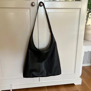 Svart axelväska  - Basic svart axelväska med skinn material men inte äkte skinn den är från hm så lite billigare material och bred axelrem. Den stängs med en liten metallknapp på insidan som man ser på bilden.