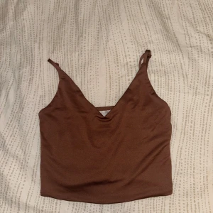 Brun croppad linnetopp med v-ringning - Säljer en brun croppad linnetopp från Amisu med smala axelband och snygg v-ringning. 