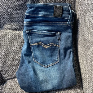 Blå Replay jeans W27 - Snygga blå jeans från Replay med klassisk femficksdesign och coola slitningar. Jeansen har en ljus tvätt och detaljerade sömmar på bakfickan. Perfekta för dig som gillar en stilren men ändå avslappnad look.