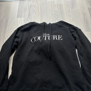 Svart hoodie från Amisu med tryck - Svart hoodie från Amisu med vit text 'Viva Couture' på bröstet. Tröjan har huva med snörning och långa ärmar. Mjuk och skön, perfekt för chill dagar. Klassisk passform och enkel stil som funkar till det mesta.