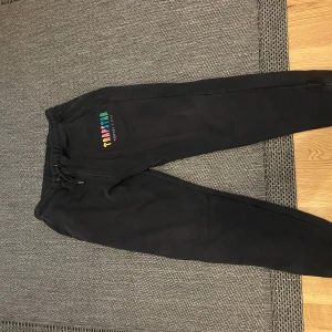 Trapstar Candy Flavours Edition mjukisbyxor - Svarta mjukisbyxor från Trapstar Candy Flavours Edition med färgglad broderad logga på vänster lår. Byxorna har snörning i midjan och är tillverkade i mjukt bomullsmaterial. Perfekta för en chill och avslappnad stil.