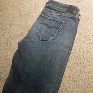 Blå Replay jeans med slitning, W29 L32 - Säljer ett par blå jeans från Replay med snygg slitning på ena benet. Klassisk femficksmodell med dragkedjegylf och Replay-logga på bakfickan. Jeansen har en rak passform och är tillverkade i mjukt denimtyg.