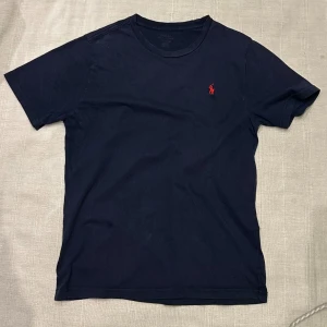 Marinblå t-shirt från Polo Ralph Lauren - Snygg marinblå t-shirt från Polo Ralph Lauren med klassisk röd broderad logga på bröstet. T-shirten har rund halsringning och korta ärmar. Tillverkad i mjuk bomull för en skön känsla och stilren look.