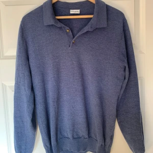 Blå pikétröja i ull från John Henric - Snygg blå pikétröja från John Henric i mjuk ull. Tröjan har klassisk krage, knappar framtill och långa ärmar. Perfekt för dig som vill ha en stilren och bekväm look till vardags. Passar lika bra till jeans som till chinos.