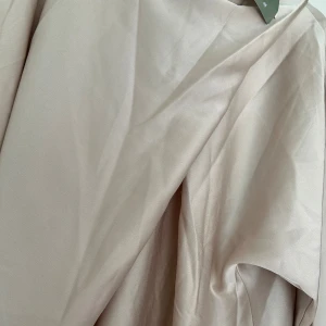 Beige långärmad klänning från H&M - Säljer en stilren beige klänning från H&M med lång ärm och rak passform. Klänningen har en mjuk, slät yta och är tillverkad i polyesterblandning. Perfekt för dig som gillar minimalistisk och clean look.