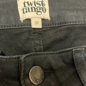 Svarta jeans från Twist & Tango, stl 27 - Svarta stretchiga jeans från Twist & Tango i klassisk femficksmodell. Jeansen har raka ben avsmalnande nertill bälteshällor och knapp med logga framtill. Snygg och enkel design som passar till det mesta. Materialet är mjukt och följsamt för en bekväm känsla.