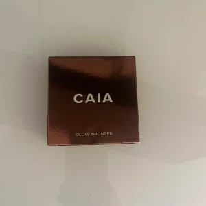 CAIA Glow Bronzer Gold Coast - Snygg bronzer från CAIA i nyansen Gold Coast. Kommer i en lyxig, spegelblank brun förpackning med spegel i locket. Pudret har en varm, gyllene ton och en vågig, cirkelformad yta. Perfekt för att ge ansiktet en solkysst glow. Helt oanvänd jag köpte fel färg 