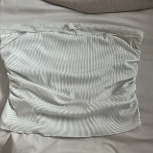 Vit ribbad tubtopp med spets och rosett - Supersöt vit tubtopp med ribbat tyg, spetskant upptill och en liten rosett framtill. 🤍